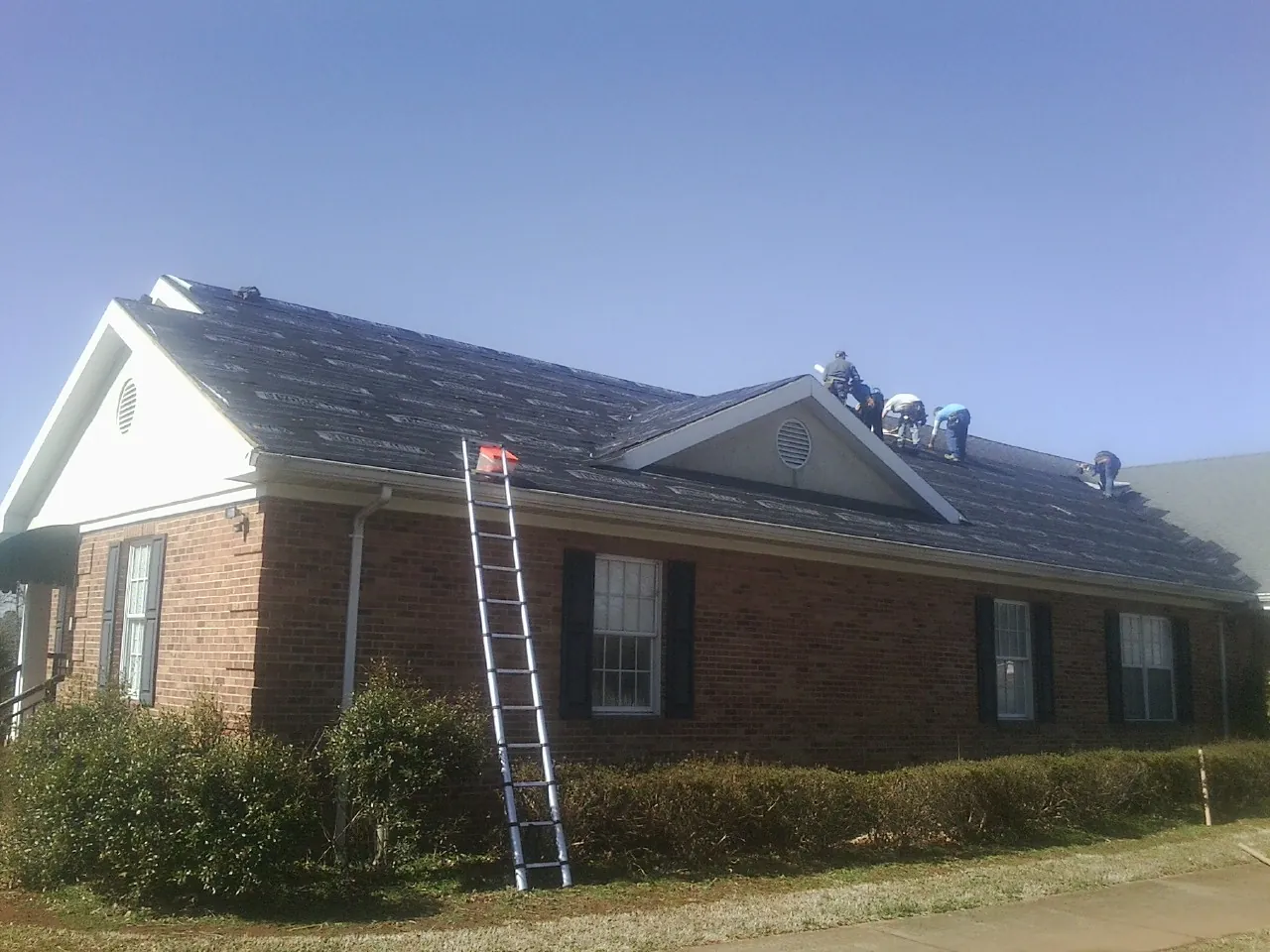 Crew tearing shingles off a brick ranch roof with a ladder set — Emergency Roof Repair work by our crew in Spangle