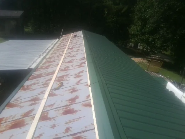 Old rusted panels beside newly installed green metal roofing — Wind Damage Roof Repair by Roofing Brothers in Spangle