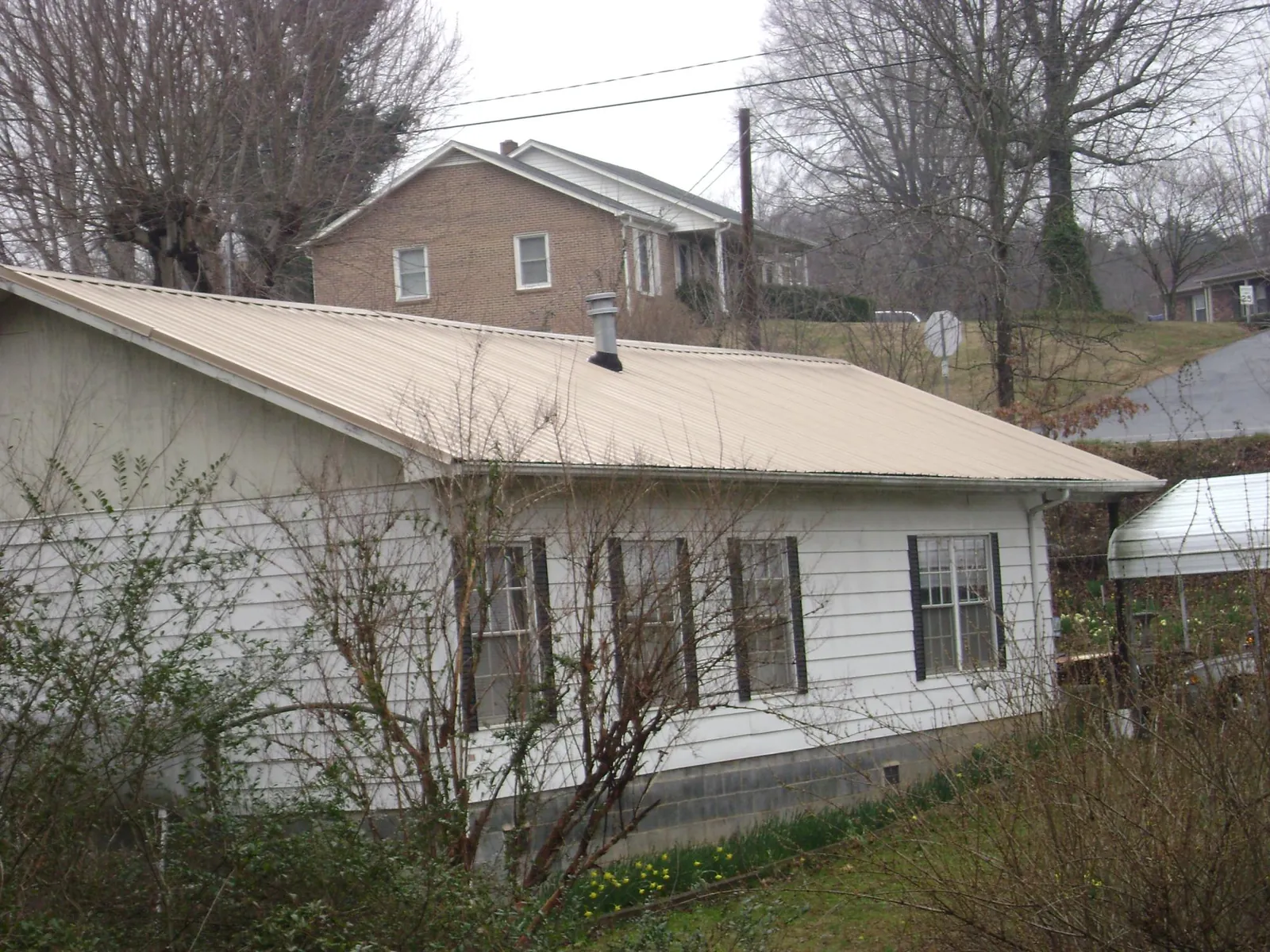 Tan metal roof on a white sided house set into a hillside — Commercial Roofing by Roofing Brothers in Spangle